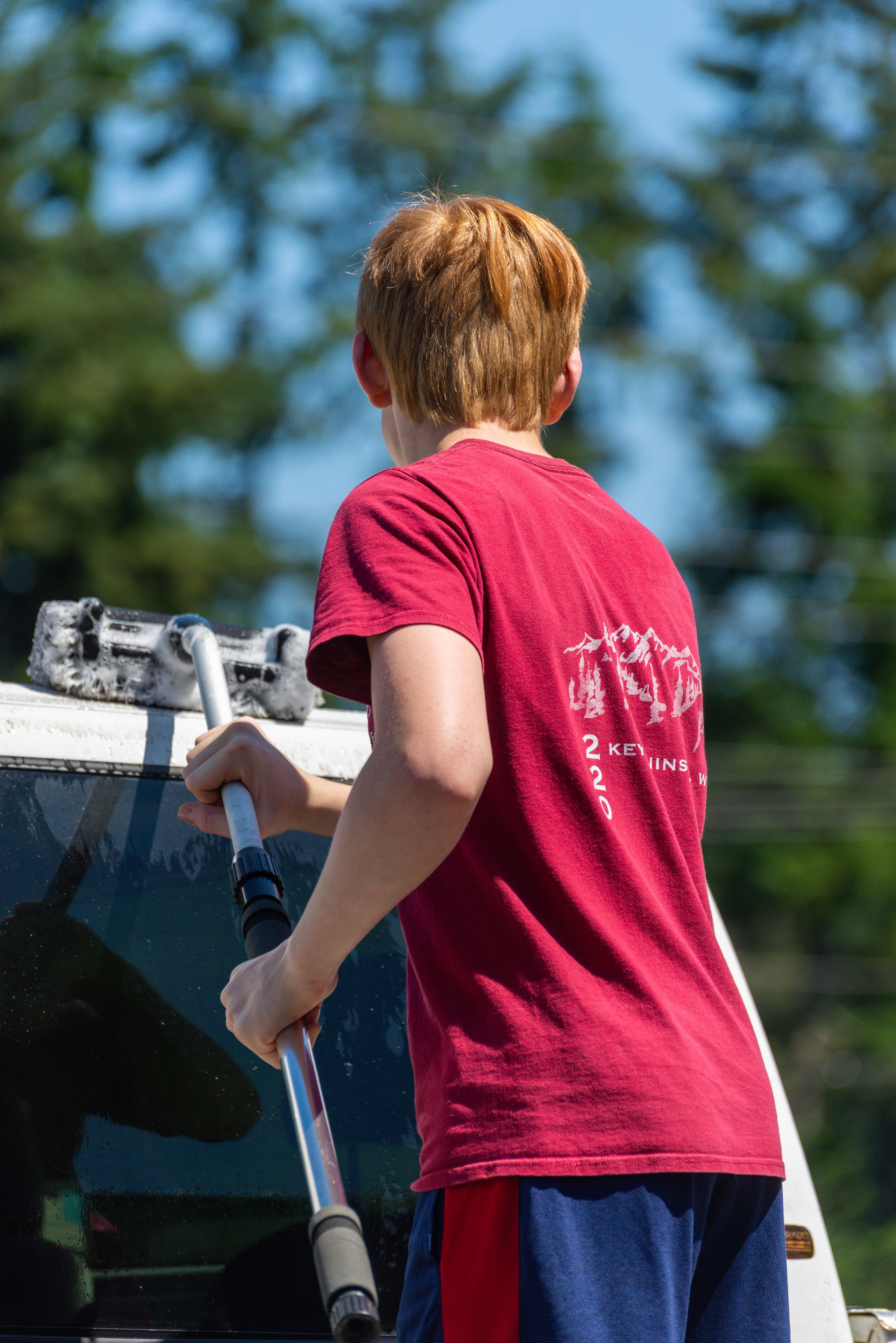 A teenager earning money by washing a neighbor's car in a driveway